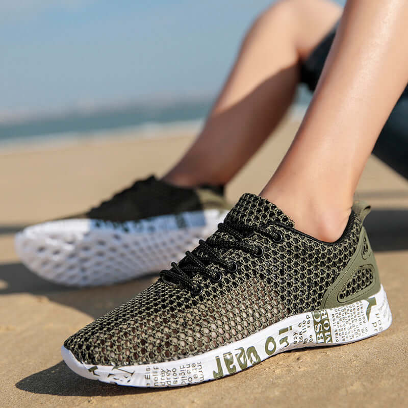 Men's breathable sneakers in dark green and black on a sandy beach, featuring a lightweight and breathable design.