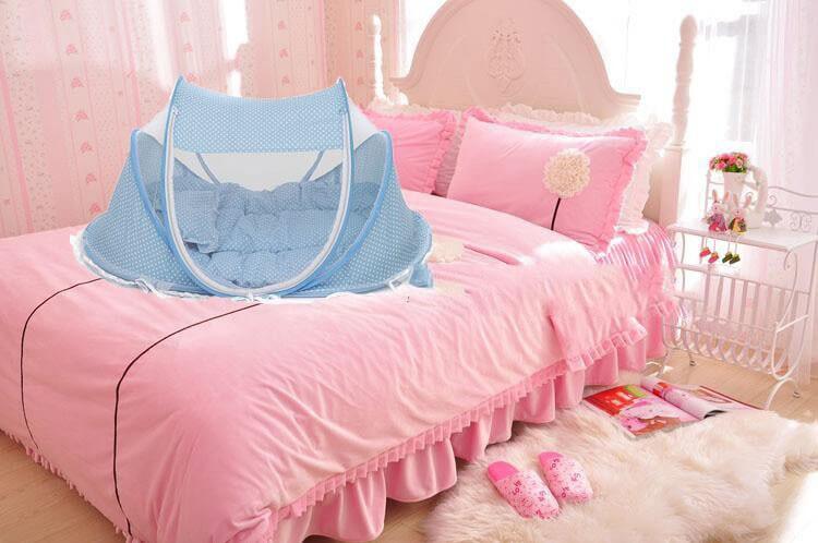 Portable baby mosquito net bed on a pink bedspread, providing a safe space for infants to sleep.
