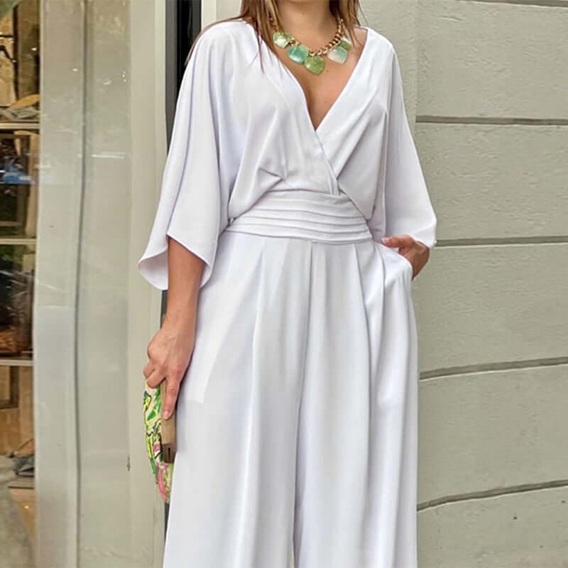 Model wearing a stylish white v-neck jumpsuit with a statement necklace, showcasing a fashionable minimalist design.