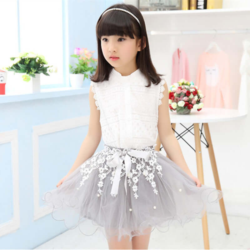 Girl wearing a fashionable lace dress with a sleeveless top and a tulle skirt, decorated with flowers and pearls.
