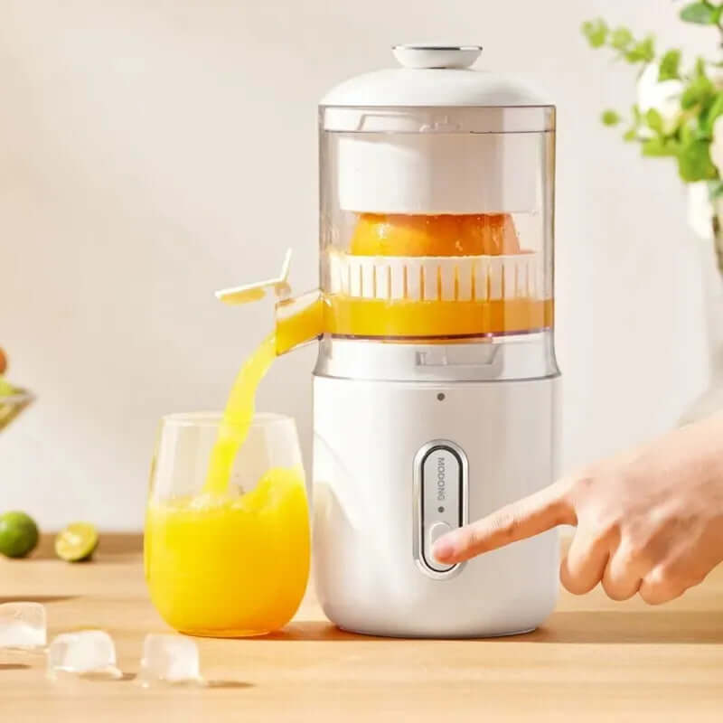 Wireless electric orange juicer pouring fresh juice into a glass with a hand pressing the button.