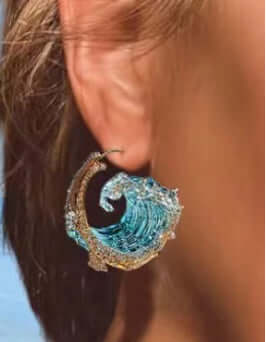 Blue wave earrings hanging on a woman's ear, showcasing intricate design and ocean-inspired aesthetics.