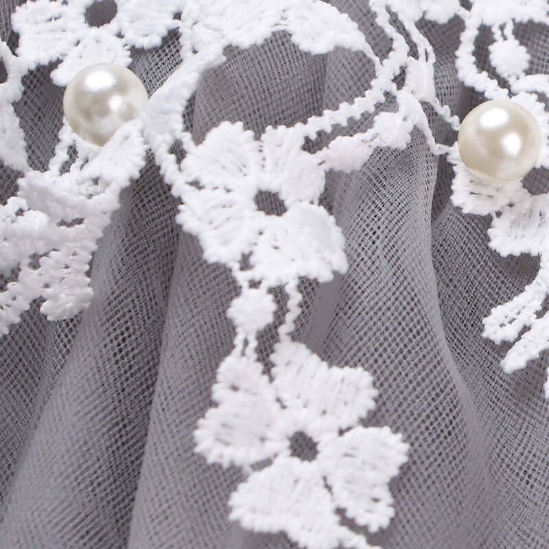 Fashion lace dress lace detail with floral patterns and pearls on a gray fabric background.