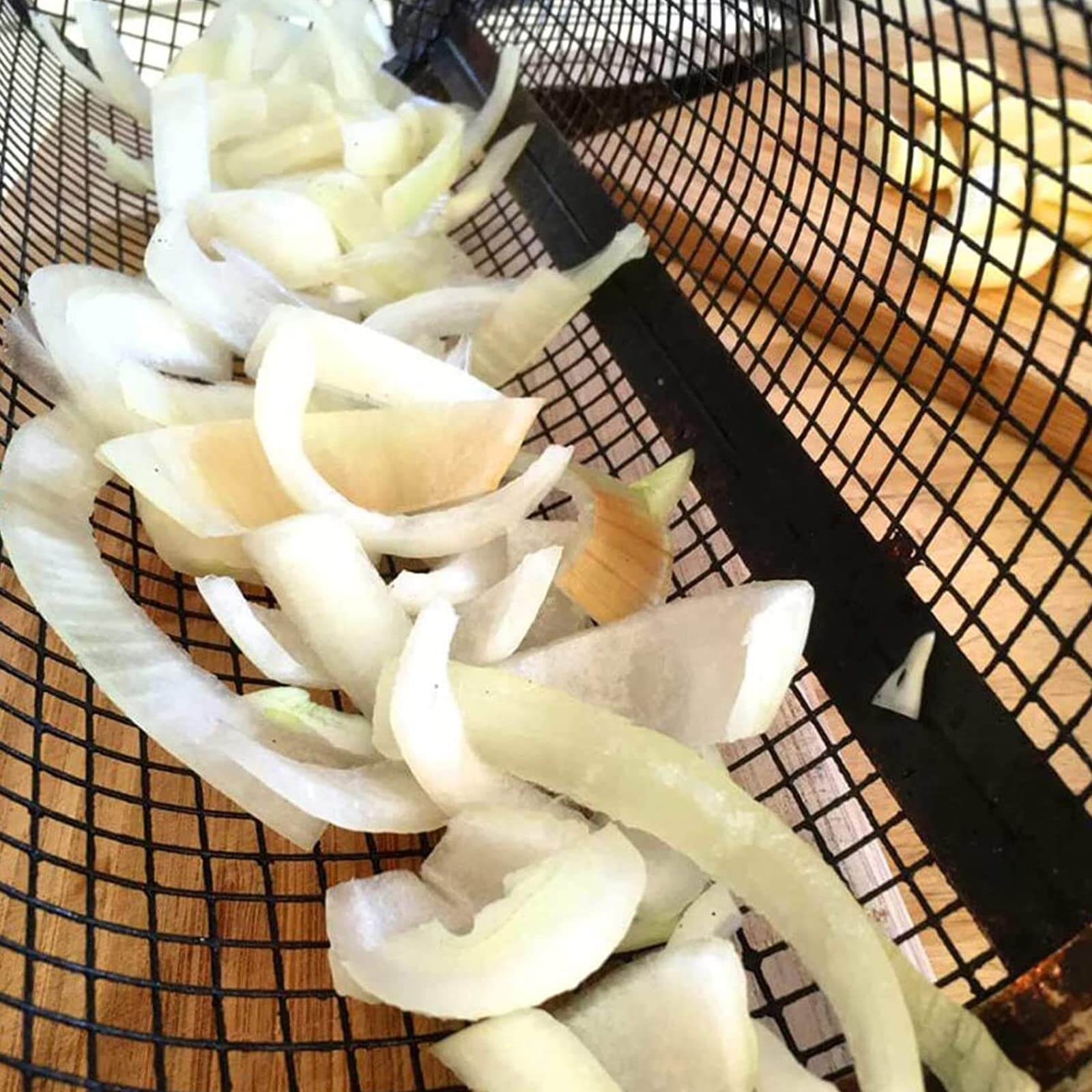 Sliced onions in a stainless steel grill basket ready for cooking on the BBQ grill.
