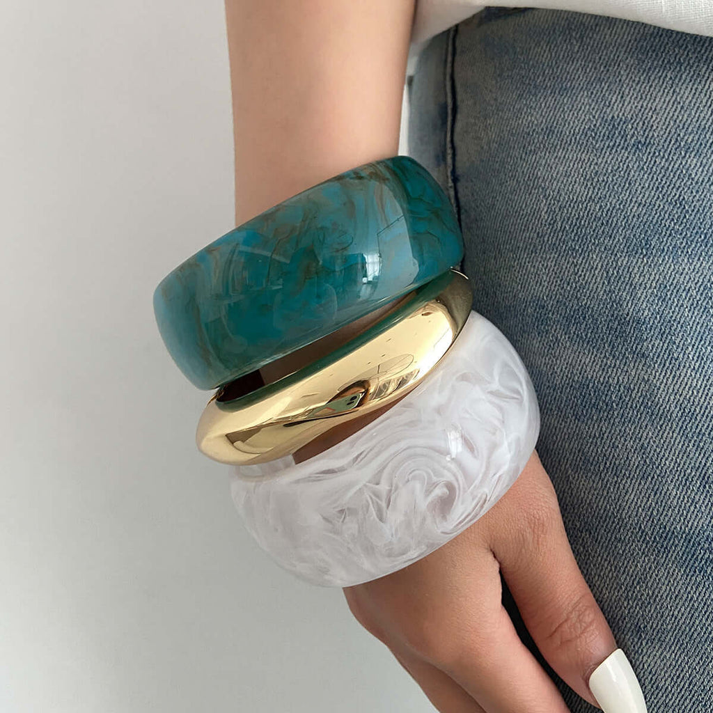 Handcrafted resin-dyed bracelet in vibrant colors stacked with gold and white bangles.