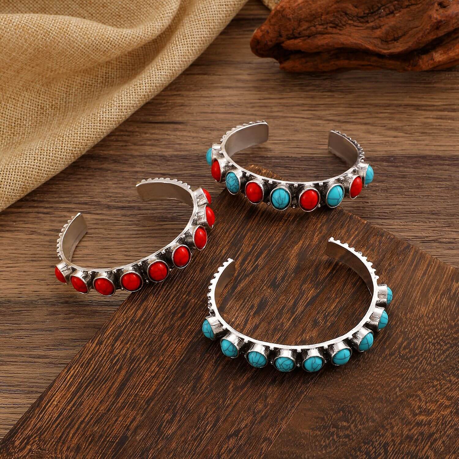 Ring-shaped electroplated bracelet trio featuring red and blue stones on wooden surface.