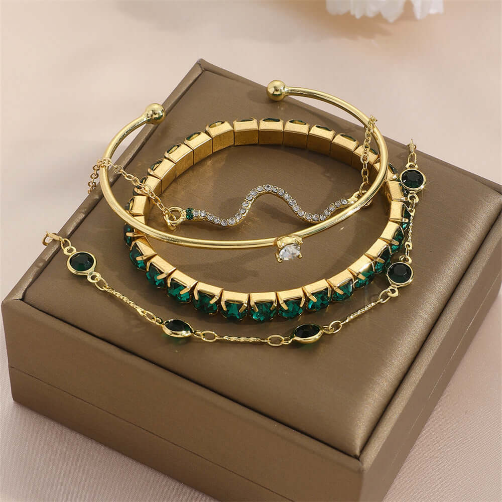 Stylish snake bracelets displayed on a jewelry box, featuring gold and green designs.