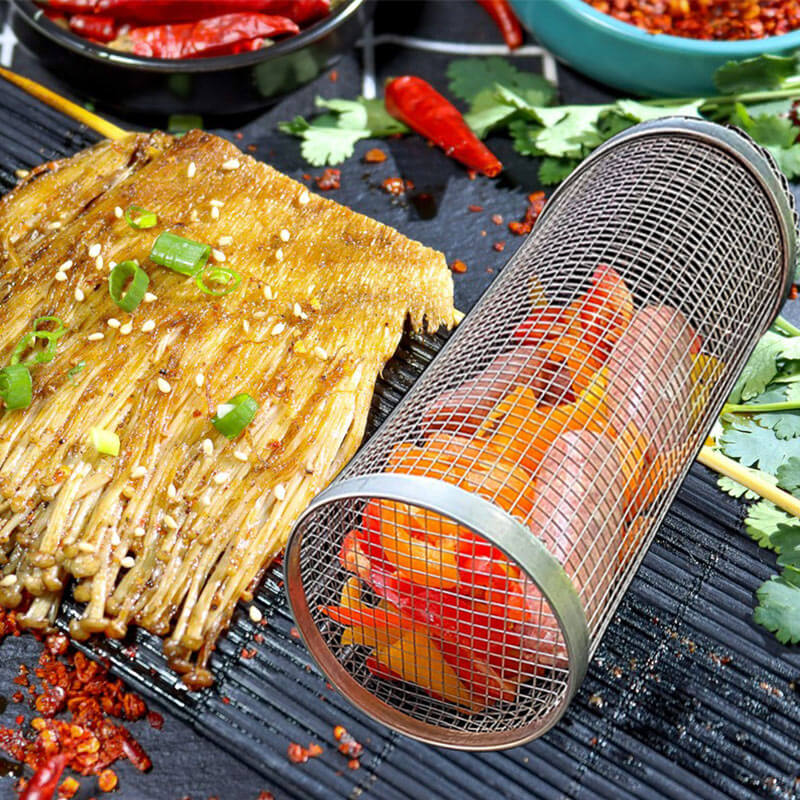 Stainless steel grill basket with diced vegetables on the grill alongside grilled fish and spices.